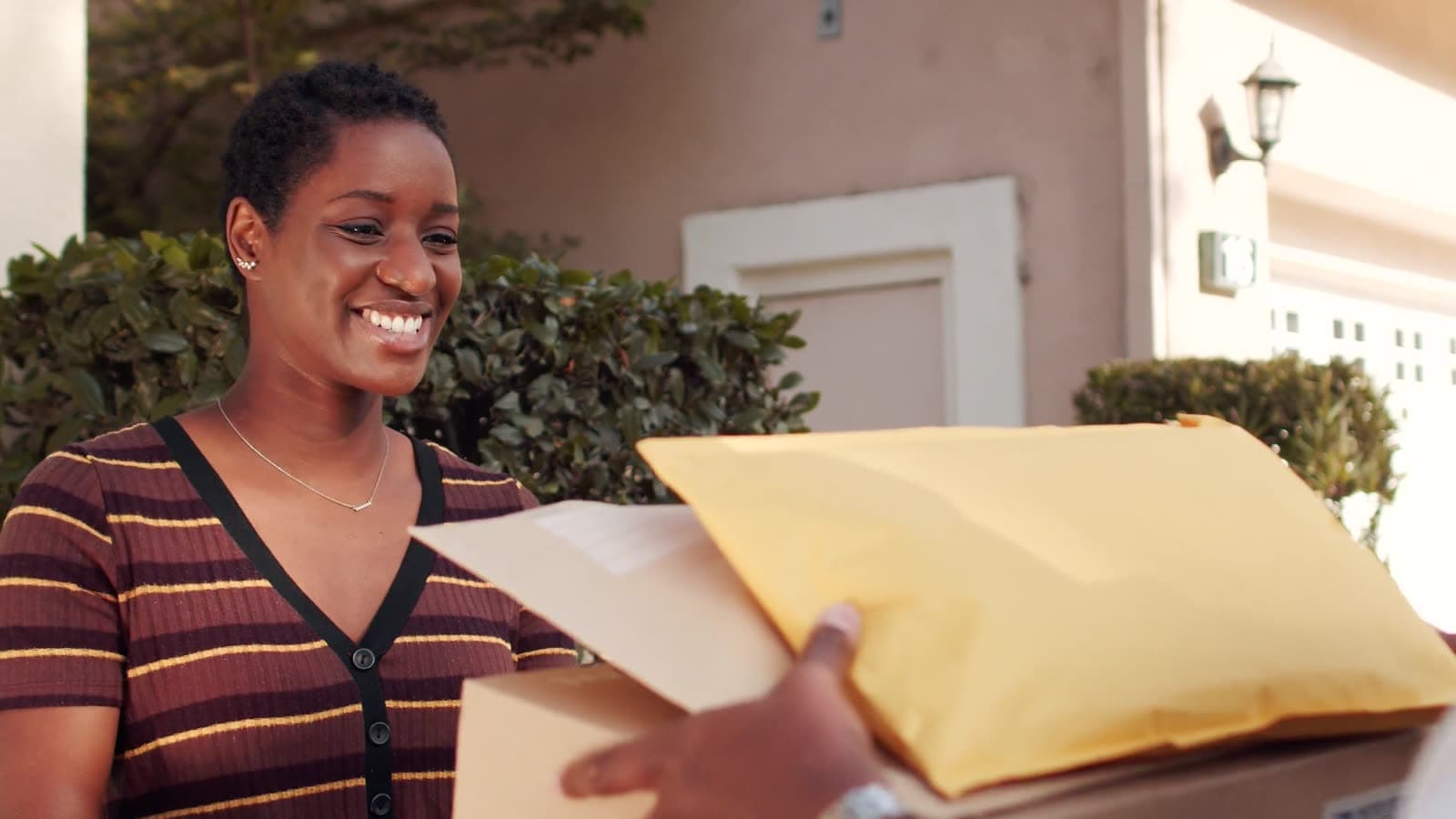 A woman smiling as she receives two parcels at her front door